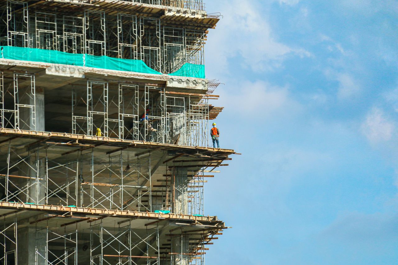 service-02 A construction worker stands on a scaffolding at a high-rise building under a blue sky.